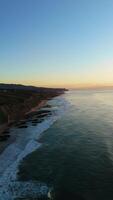 magoito playa y acantilados a puesta de sol durante bajo marea. atlántico océano, Portugal. dorado hora. aéreo vista. Moviente hacia atrás. vertical video