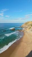 adraga playa y acantilados en soleado día. atlántico océano, Portugal. aéreo vista. orbital. vertical video