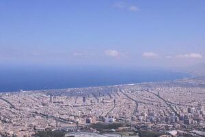 Coastal city aerial view, clear sky, ocean horizon, urban sprawl, travel brochure photo