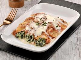 Baked SPINACH CANNELLONI with sauce and fork served in dish isolated on wooden table side view of italian fast food photo