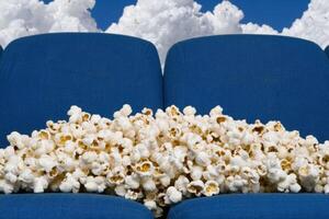 A big pile of popcorn sits on a blue couch in front of a cloudy sky photo
