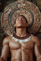 Shirtless muscular man meditating in front of ancient Mayan stone carving photo