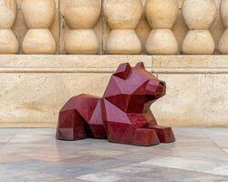Geometric red bear statue in front of a stone wall photo