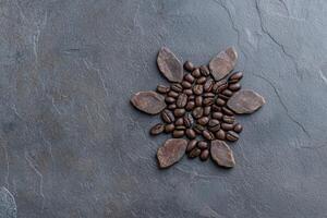 Coffee beans arranged in a sunburst pattern with cocoa pieces on a dark gray slate background photo