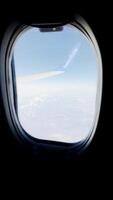 airplane wingtip framed in a window view above clouds and blue sky. Serene horizon, peaceful atmosphere, scenic aerial perspective, modern flight, and global travel video