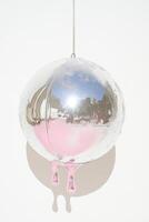 Artistic glass sculpture with a reflective surface and soft pink hues hanging against a white background. photo
