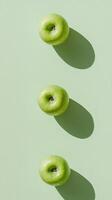 Three fresh green apples casting shadows on a light green background create a minimalist and natural composition. photo