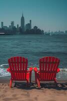 Two vibrant red chairs on a sandy beach, overlooking a bustling city skyline under a clear blue sky. photo