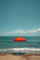 A vibrant red umbrella offers shade on a sunny beach day by the ocean. photo