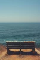 A solitary weathered bench overlooks the vast ocean under a clear blue sky. photo