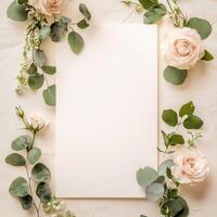 Blank white card surrounded by soft pink roses and greenery on a textured surface. photo