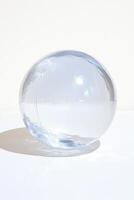 Minimalistic clear glass sphere casting a shadow on a white surface. photo