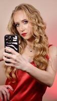 A young woman with red lipstick takes a selfie with long blond hair and makeup. The girl is smiling and looking at the camera close-up photo