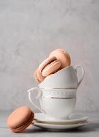 Mocha Mousse - color of the year 2025. Stack of white coffee cups filled with macaroons on the edge of the table, white brick wall background photo