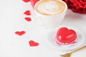 red heart shaped cake and coffee for valentines day on white table setting, copy space photo
