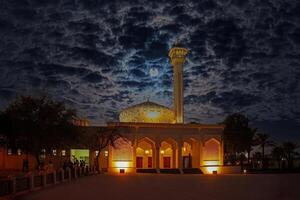 Illuminated mosque under dramatic cloudy night sky with glowing full moon photo
