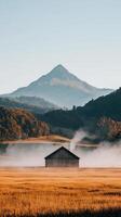 A serene mountain landscape featuring a misty field and rustic barn under a clear sky. photo
