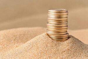 Stack of coins emerging from a sandy surface, representing wealth and investment. photo
