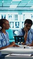 Vertical Group of healthcare specialists in scrubs analyzing results with doctor, emphasizing teamwork, professional training and care management in a modern office. Medical staff doing research. Camera B. video