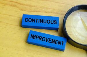 Top view of continuous improvement text on blue wooden blocks with magnifying glass background. Continuous improvement concept photo