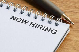 Now hiring text on white notepad. Recruitment and hiring concept photo