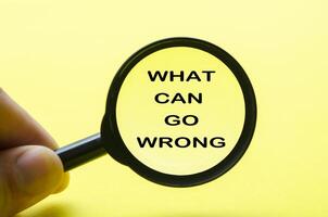 Hand holding magnifying glass with text what can go wrong. Fact finding concept. photo