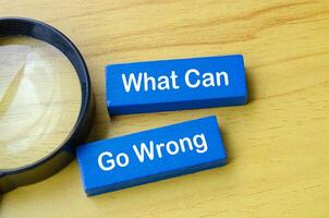 Top view of What Can Go Wrong text on blue wooden blocks with magnifying glass photo