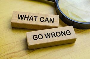 Top view of What Can Go Wrong text on wooden blocks with magnifying glass. Auditing concept. photo