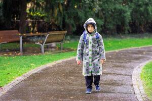 A child in a raincoat with a school bag goes to school in the rain. photo