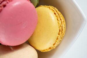 small multi-colored macaroons in a white plate on a white background. photo