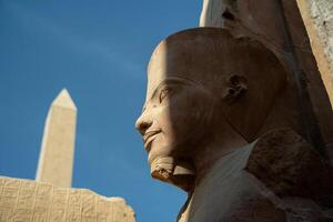 Statue of a pharaoh with an abelisk in the background in Luxor photo