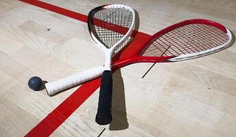 Two rackets and two squash balls lie on the parquet floor. Horizontal photo