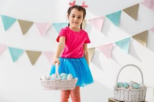 Getting ready to Easter. Lovely little girl holding an Easter egg and smiling with decoration in the background photo