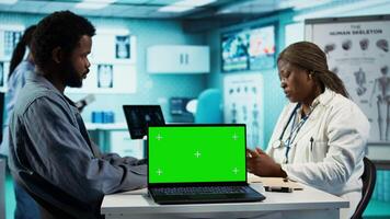 African american young man asking his medic practitioner about advice next to mockup, analyzing the medical records together at checkup. Physician meeting with ill patient. Camera B. video