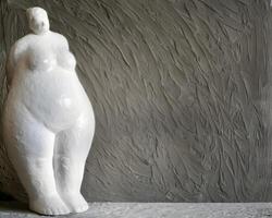 A figurine of a plump woman made of white plaster against a gray background with copy space in a minimalist style. photo