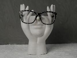 Glasses with a black frame in a white dot on a white headless figurine made of stone on a gray background photo