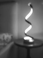 A spiral-shaped lamp on a black bedside table in the style of a blurred black-and-white photograph, Suitable for text overlay photo