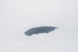 Frozen ice hole, a spot of ice on white snow. White winter minimalistic landscape with round backwater with blue ice on the snow river. photo