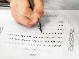 Close-up pupil's hands are writing calligraphy in a notebook. Schoolboy calligraphy performs a task at the workplace. Concept of children's education, teaching knowledge, skills and abilities. photo