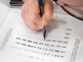hands are writing calligraphy in a notebook. Schoolboy calligraphy performs a task at the workplace. Concept of children's education, teaching knowledge, skills and abilities. photo