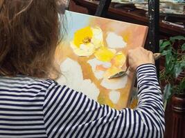Creative woman drawing texture paste, working with a spatula, creating a three-dimensional drawing of flowers in the picture. photo