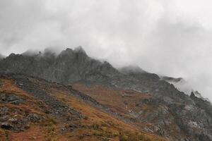 Mystical background with dramatic mountains. Rain in mountains. Atmospheric misty landscape with fuzzy silhouettes of sharp rocks in low clouds during rain. photo