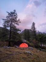 Twilight summer camp in the mountains. Amazing scenery of twilight in mountains with tent on pass in violet light. Tent near rocky hill in lilac light. Purple sunset light. photo