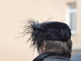 Back view of the woman with black hat with feathers on the head in a open air photo