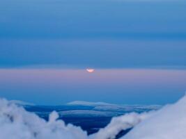 Moon partly hidden behind clouds. Part of the full moon behind the clouds. Arctic evening sky with moon. photo