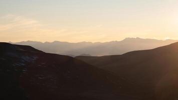 Scenic sunset mountain landscape with golden low clouds in valley among mountains silhouettes under cloudy sky. Vivid panoramic sunset or sunrise scenery in mountain valley in illuminating color. photo