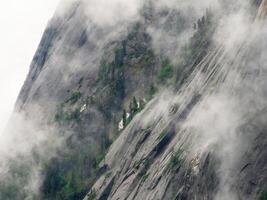 Vertical granite wall of a mountain with a tree forest above a c photo