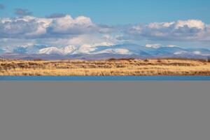 Beautiful autumn mountain lake and mountains. Reflection of snowy peaks and dry yellow grass in the steppe on the surface of a mountain lake. photo