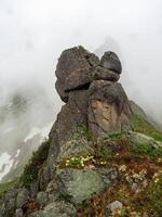Mountain vertical view from cliff at high altitude. Mystical landscape with beautiful sharp rocks near precipice and couloirs in low clouds. Mountain foggy scenery on abyss edge with sharp stones. photo