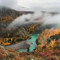 river Argut in valley with forest in autumn colors on background of foggy mountains silhouettes under low clouds. Beautiful mountain valley in autumn. photo